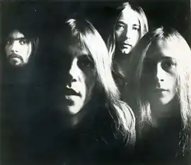 Black and white photo of four men with long hair in their late-20s in the dark