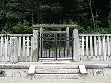 Wooden torii gate behind a stone fence in front of trees.