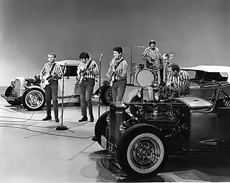 The Beach Boys performing, flanked by muscle cars