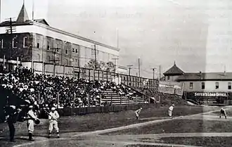 A black and white photograph of home plate and left field bleachers at a ballpark