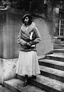 Lavaud in a hat and coat standing on the steps of a building.