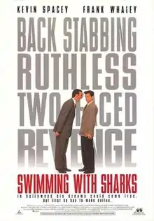 A man towering over another shouting down at him. The words "Swimming with Sharks" filling the background