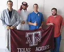 Four people standing behind a flag each holding their thumb in the air