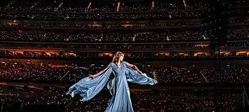 Swift dressed in a white gown, singing into a microphone.