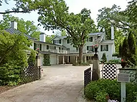 Exterior of a large, white, 3-story country house with driveway and gate