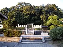 Torii gate behind a white stone fence in front of trees.