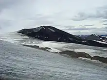 A black cone-shaped mountain rising over glacial ice.