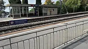 Double-track railway next to a lake with canopy-covered shelter on platform