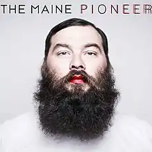 An adult man with a bushy beard, red lips and a white shirt is front-and-centered on the grey cover. The band name appears above the man, along with the album title that's colored twice: one in black and one in red over it.