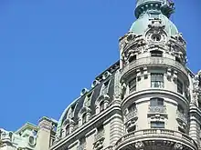 Detail of a cupola at one of the building's corners. The cupola has black slate tiles and green copper cresting. There are windows below the cupola.