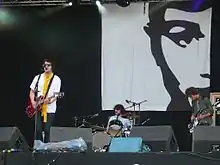 Three men onstage playing instruments and singing into a microphone