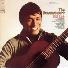 A smiling man holds a guitar. He is dressed with a green shirt and a black turtleneck. To his right, the title of the record is featured and tracks are listed