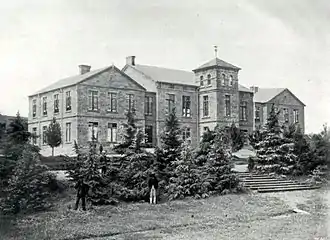 A black and white photograph of a large mansion house, surrounded by various trees