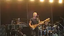 A bassist/singer, Sting, is shown at a performance. A number of speaker cabinets are shown onstage.