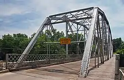 One-lane bridge with metal trusses over a wooden deck, with a pedestrian walkway on the right