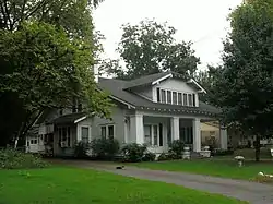 Photo of a stately one and a half-story craftsman-style home sits among mature trees behind a manicured lawn