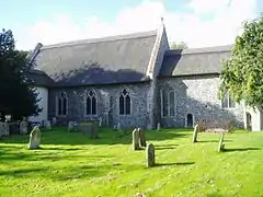 A small thatched flint church seen from the south, showing the nave and a smaller chancel