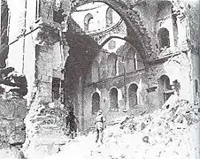 Black & white image of a lone soldier gazing at synagogue interior through a destroyed side wall