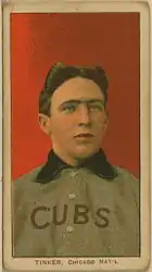 A man with brown hair wearing a grey baseball uniform with a blue collar and the word "CUBS" on his chest in front of a red background