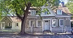 A stone house with white wood trim across a street behind a tall tree