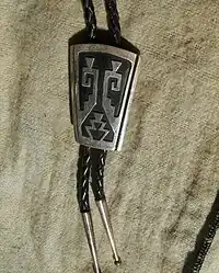 silver overlay bolo tie, by Tommy Singer, c. 1980s. This is an example of a Navajo copy of Hopi silver overlay technique, evident from the absence of matting on the black oxidized surfaces of the bottom silver sheet, or small, repeated, closely packed chisel strokes, very taxing on the silversmith, especially the eyes.