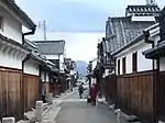 A narrow street lined by houses with a wooden lower part, a white upper storey and tile roofs.