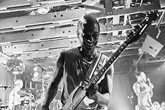 A black-and-white photograph of Tony Kanal playing the guitar live in 2017.