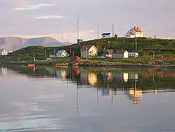 The Torsvåg lighthouse sits at the top of Kåja. The largest house is the Figenschow building, and the house on the far left is the Solberg building. Behind Kåja we can see Nordkvaløya.