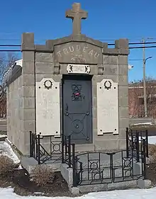 Building constructed of grey granite blocks, adorned with a cross above a metal door, and what plaques with names inscribed