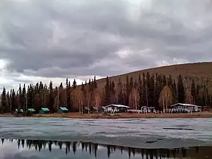 Scattered cabins are seen behind a lake with ice floating on its surface