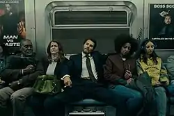 A man on a subway spreading his legs apart, squishing people beside him.