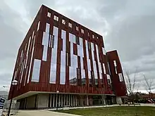 Image is a wide angle view of a modern building with long windows and terracotta siding.