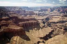 Wide canyon with steep tan colored walls. A river inside a valley is below a broad gently sloping surface.