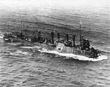 Three-quarter overhead view of destroyer with four funnels and damaged bow, at sea