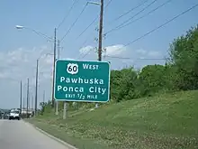 A large green road sign, reading "US-60 West/Pawhuska, Ponca City/Exit ½ Mile"