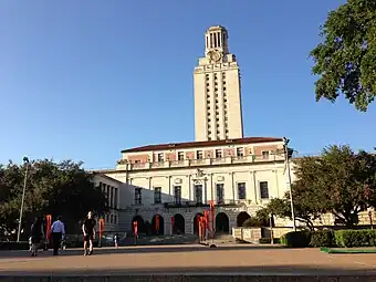 An early 1900s gothic-revival-style long building can be seen with a tall clock tower rising above it.