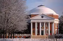 A red brick, Neoclassical dome with a large portico on the front and covered walkway on the sides. Snow covers the foreground and trees.