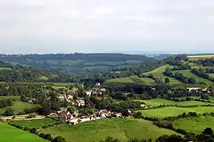 The roofs of several houses can be seen nestling in a green valley with lots of trees.