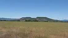 Upper Table Rock from across a field of grass, looking into the central bowl. It rises steeply from the surrounding valley to its flat top.