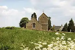 Stone building with tower beyond field and stone wall.