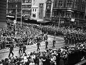 Crowd of people watching a parade of military personnel march along a city street