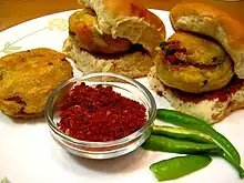 One batata (potato) vada, two vada pavs, raw green chillies, and seasoning of red garlic chutney.