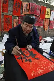 A Vietnamese calligrapher is writing 祿 (read as "lộc", means "good fortune") in preparation for Tết at the Temple of Literature, Hanoi