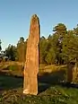 A small and tall runestone with red inscriptions.