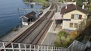 Double-track railway next to a lake with two-story station building at right