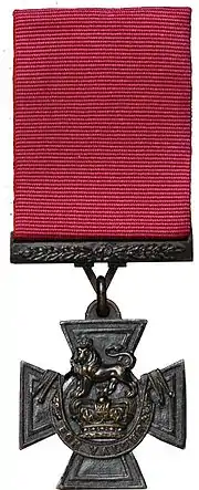 A bronze Cross pattée suspended from a crimson ribbon