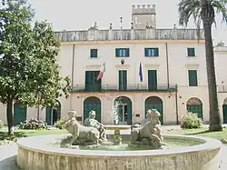 A water fountain with statues in front of a large home.