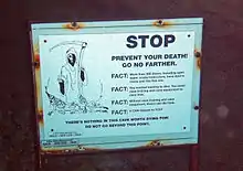 A white warning sign with a picture of the [Grim Reaper] and the headline "Prevent your death. Go no farther" over black text explaining the dangers to divers of proceeding into the cave without proper equipment and certification