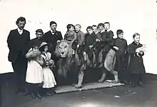 Black and white photo of children standing around and sitting on top of taxidermied lion