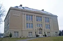 A large square beige-colored three-story brick building with pilasters on the front and the words "Washington School" engraved below the roof. Between the windows on the second and third stories are the words "science" "language" and "history".